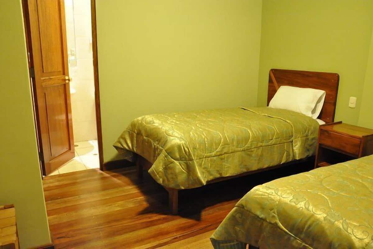 Una habitación con dos camas, piso de madera y una puerta que da a otra habitación.
