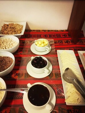A table with various food items including bowls of grains, a cup of coffee, and a plate with sliced cheese. - Killa Qente Cusco Hostal (Cusco)