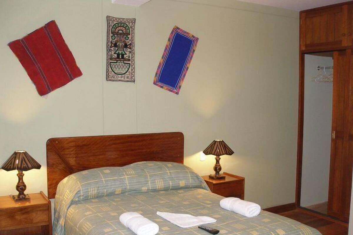 Habitación de hotel con una cama, dos mesitas de noche con lámparas, un armario de madera y una puerta.