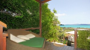 A wicker lounge chair with a green cushion on a wooden deck, overlooking a coastal landscape with trees and a view of the sea. - Pousada Pelicano (Búzios)