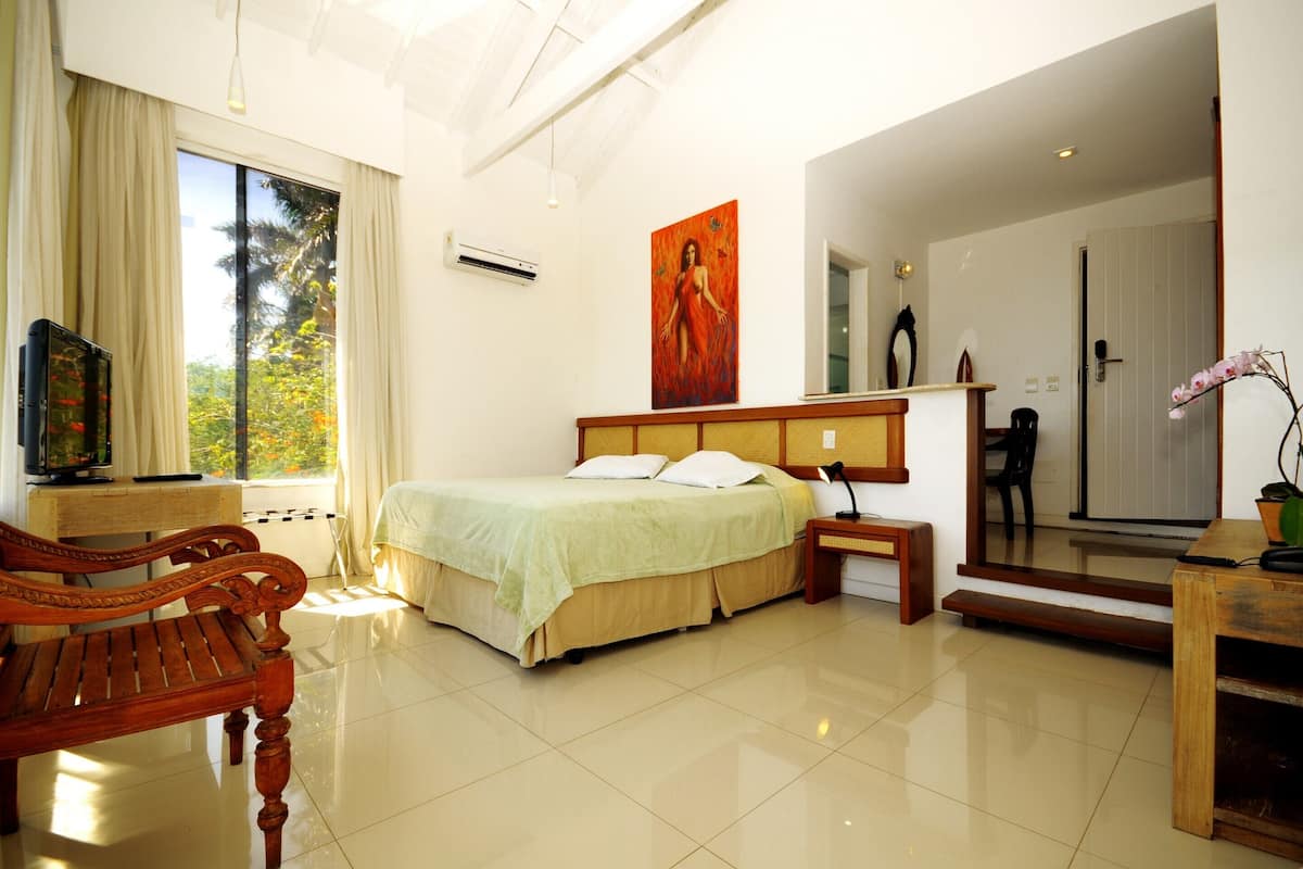 Habitación de hotel con una cama, un banco de madera, un escritorio, una silla, un cuadro y vistas al exterior.