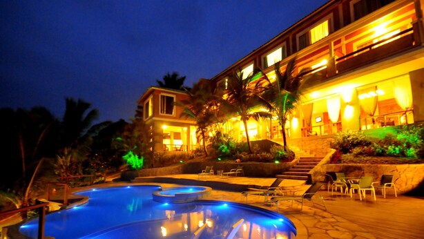 A swimming pool with lounge chairs and a building with illuminated windows and outdoor seating. - Pousada Pelicano (Búzios)