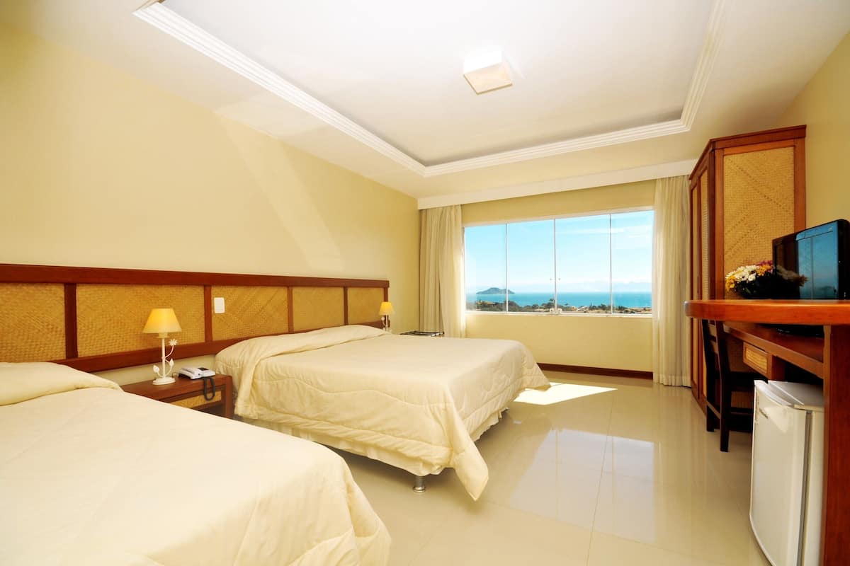 Habitación de hotel con dos camas, televisión, escritorio y vista al mar.