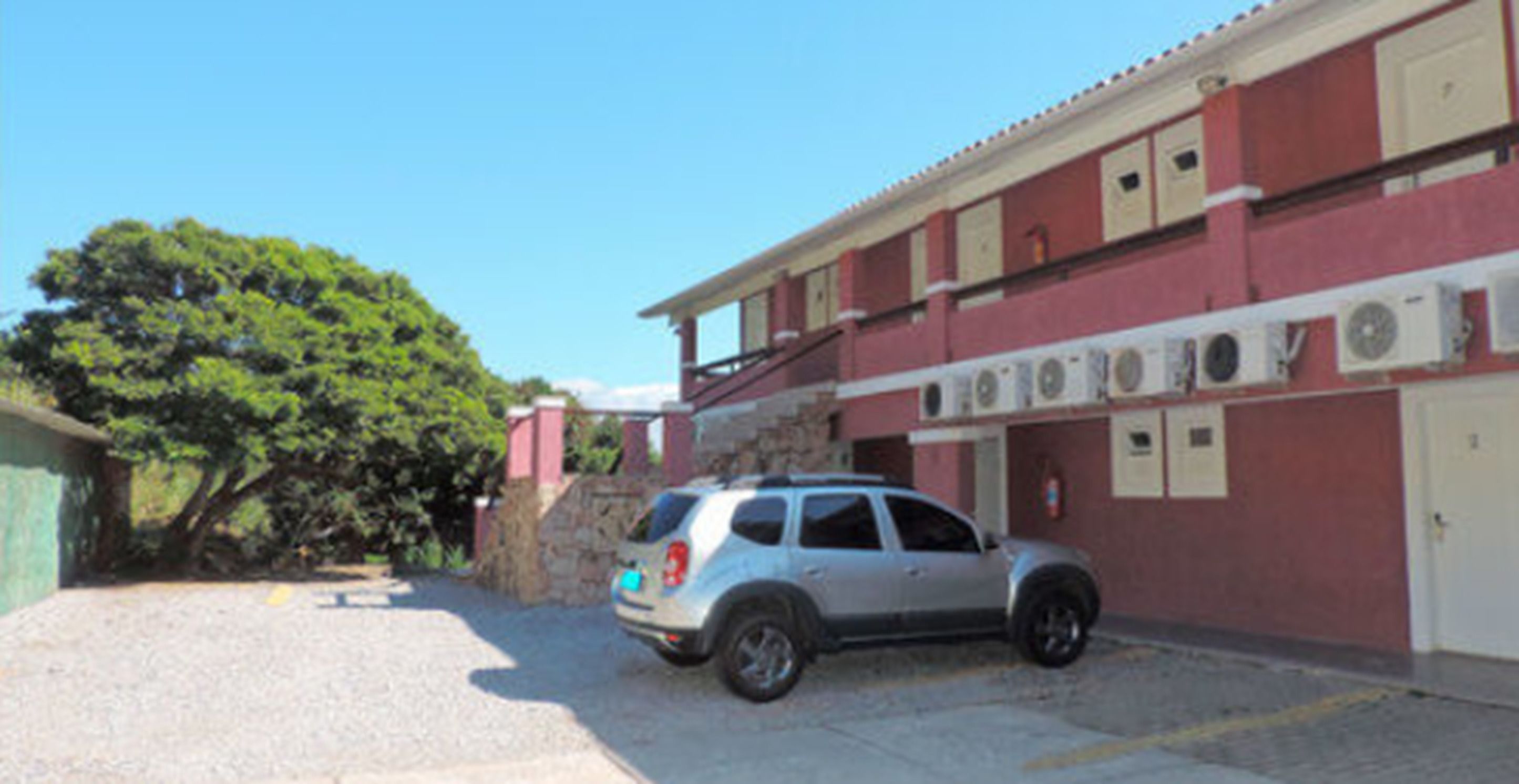 Un edificio con fachada roja, varias unidades de aire acondicionado y un SUV plateado estacionado.