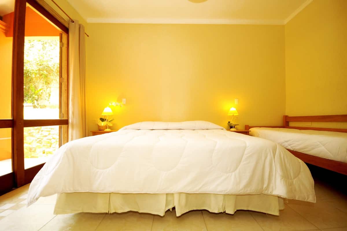 Una habitación de hotel con una cama grande, dos mesitas de noche con lámparas y un ventanal con cortinas.