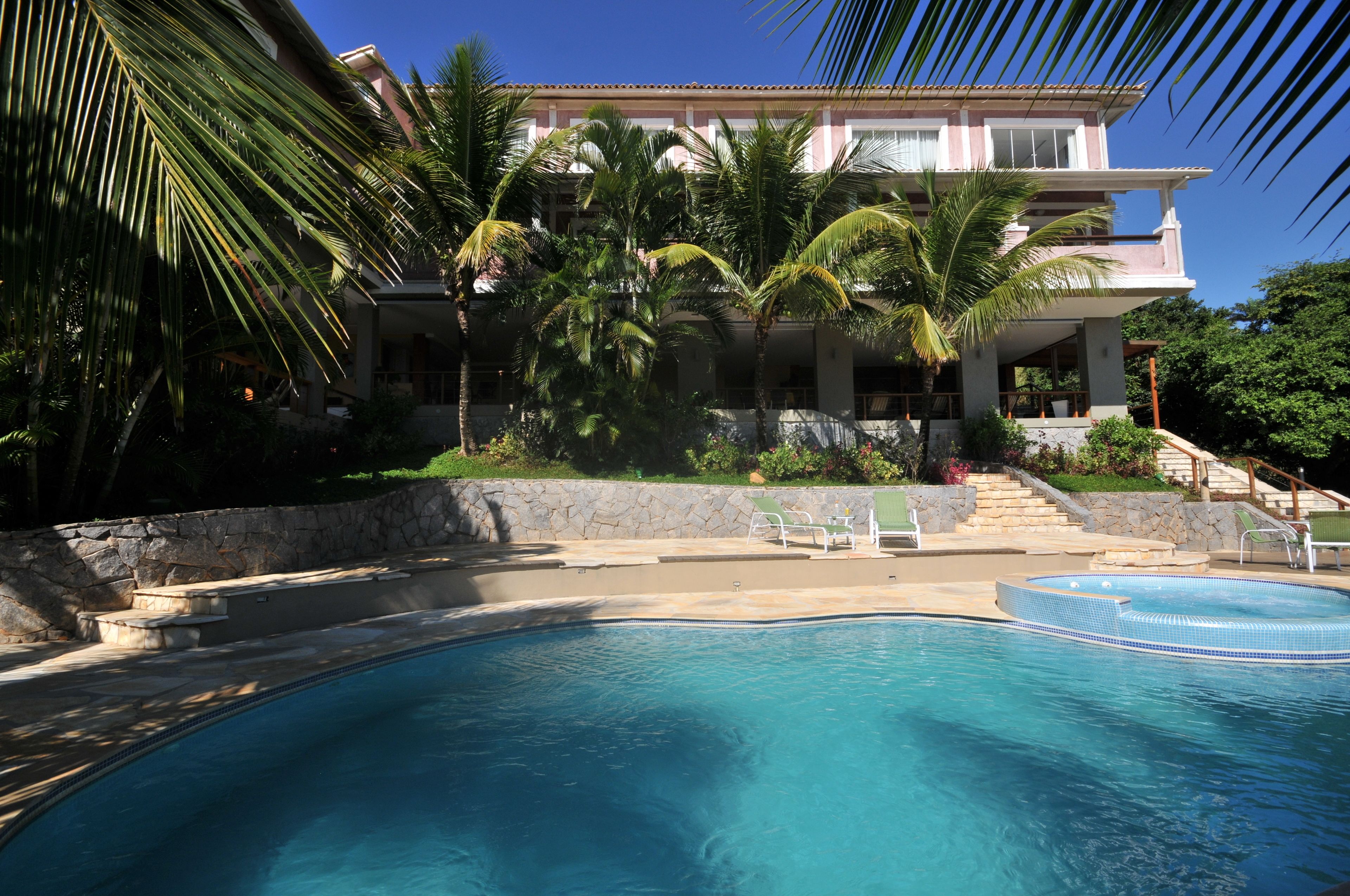 A swimming pool with a stone wall and palm trees, a stone staircase, and a building with balconies.