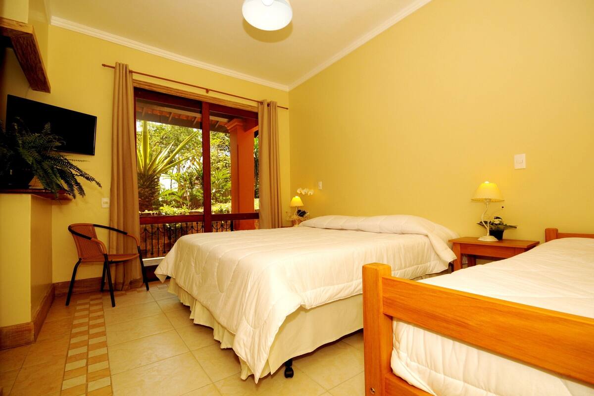 Habitación de hotel con dos camas, televisión, una silla y balcón con cortinas.