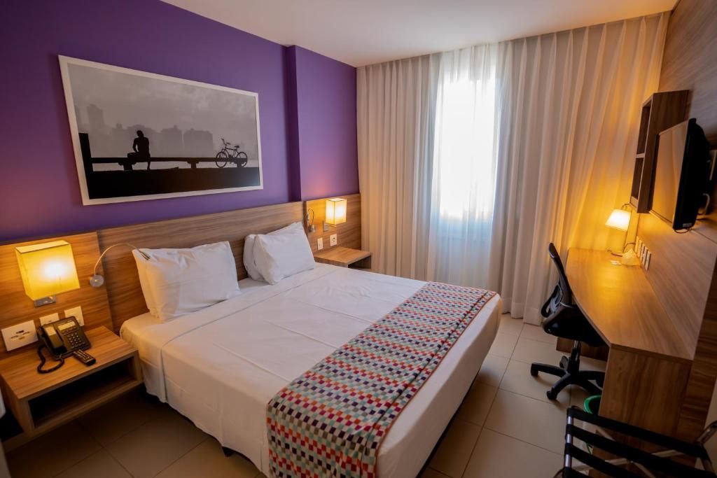Habitación de hotel con una cama grande, lámparas de noche, un escritorio y un televisor.