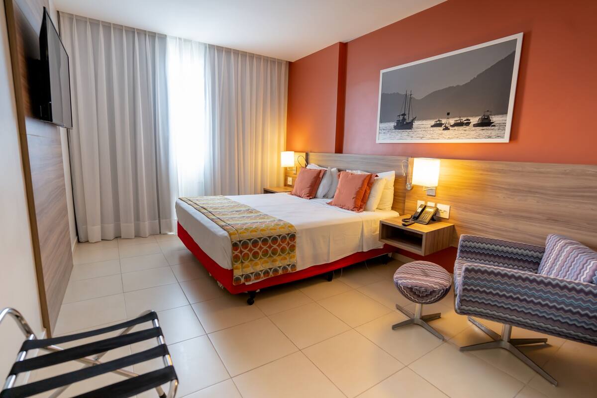 A hotel room with a bed, bedside lamps, a TV, a chair, and a sofa.