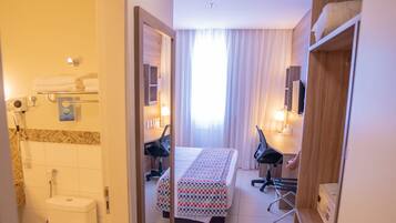 A hotel room with a bed, desk, chair, and a bathroom with a toilet and shower.