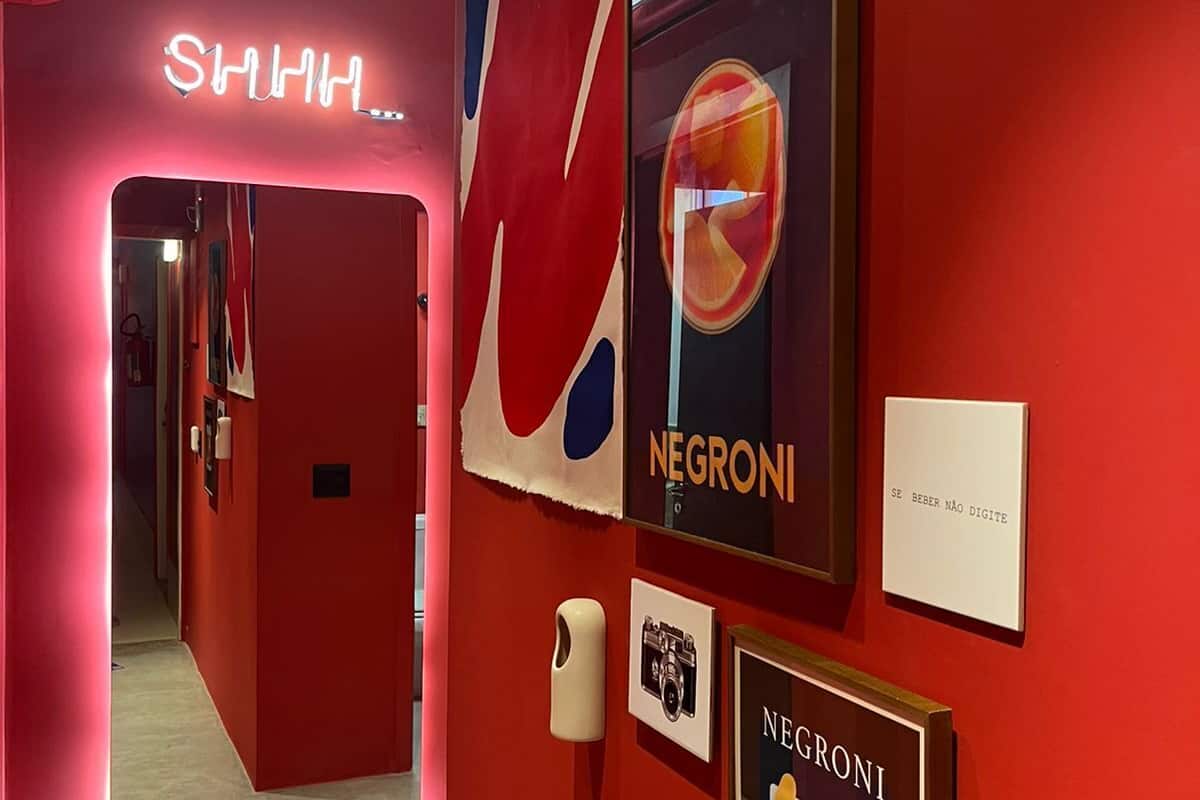 A red-themed interior with a neon sign reading "SHHH..." and multiple framed artworks on the walls.