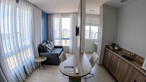 A modern hotel room with a dining table, a sofa, a kitchen area, and large windows offering city views. - Comfort Hotel Santos (Santos)
