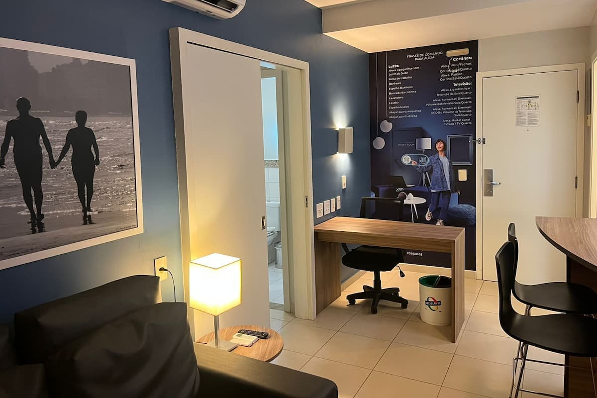 A hotel room with a bed, a desk, a chair, a lamp, and a poster on the wall.
