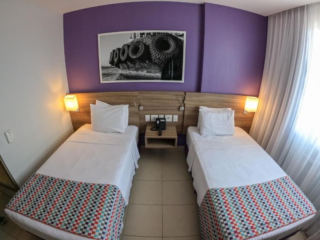 Una habitació d'hotel amb dos llits, un capçal amb un telèfon i un quadre penjat a la paret.