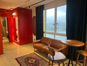 A modern living room with a leather sofa, a round wooden table, and a view of a cityscape through large windows. - Comfort Hotel Santos (Santos)