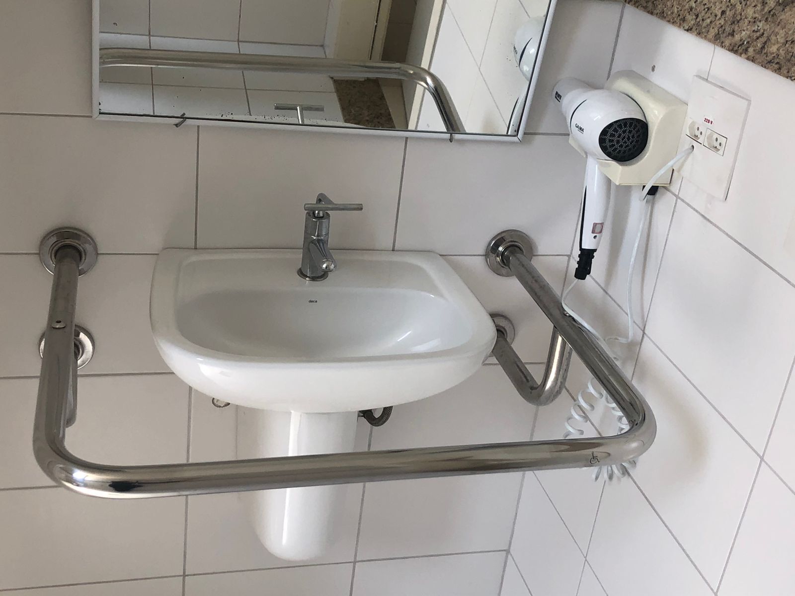 A bathroom with a white sink, a mirror, and a hairdryer mounted on the wall.