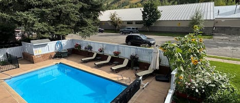 A swimming pool with lounge chairs and a white fence, surrounded by greenery and a view of a mountain.