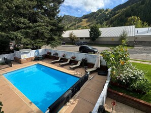 Una piscina con sillones de descanso y una valla blanca, rodeada de vegetación y con vistas a la montaña.