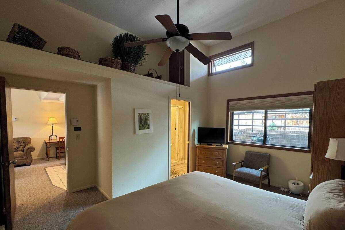 Une chambre avec un grand lit, un ventilateur de plafond, une télévision et une fenêtre donnant sur la rue.