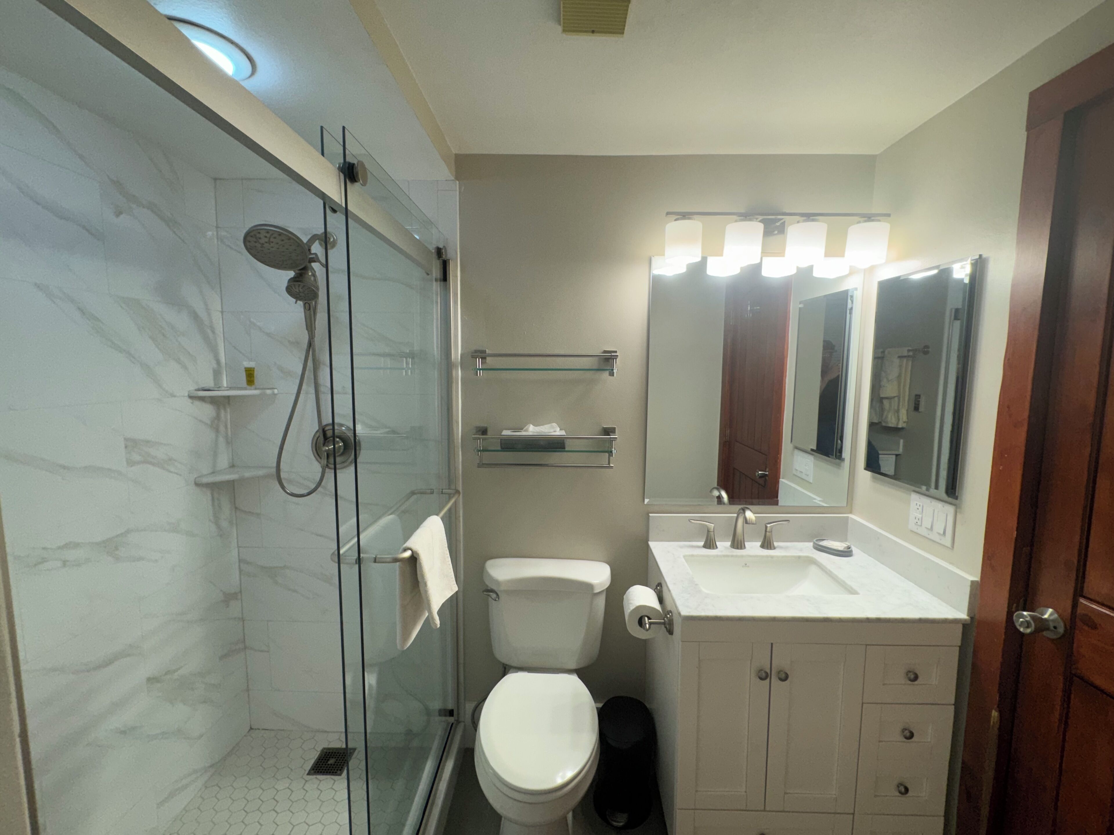A bathroom with a glass-enclosed shower, a toilet, a sink with a mirror, and a cabinet.