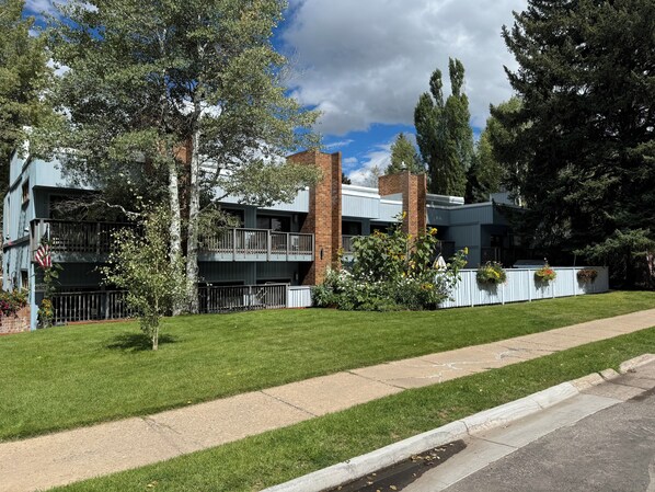 Un edificio moderno de varios pisos con fachada de ladrillo, un balcón y un césped bien cuidado.