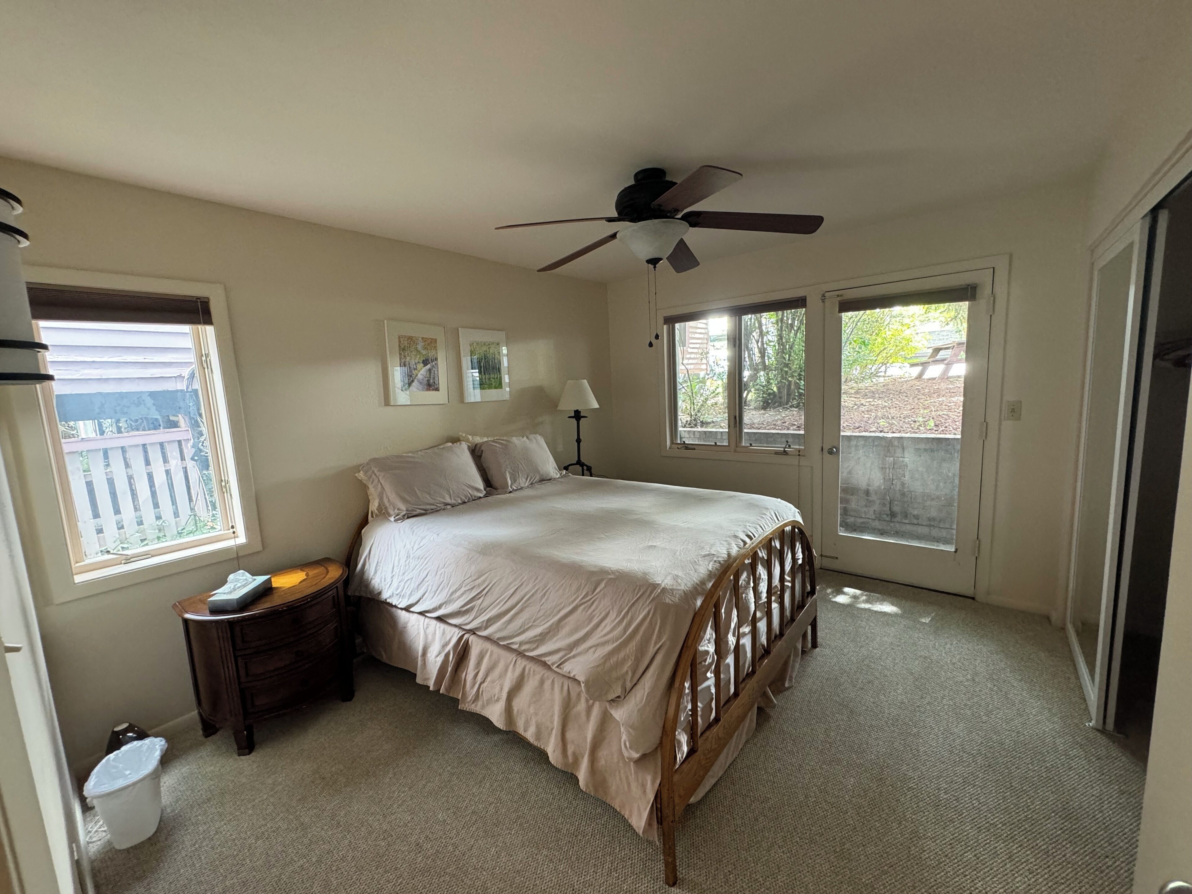 A bedroom with a bed, a ceiling fan, a nightstand, a lamp, and a window.
