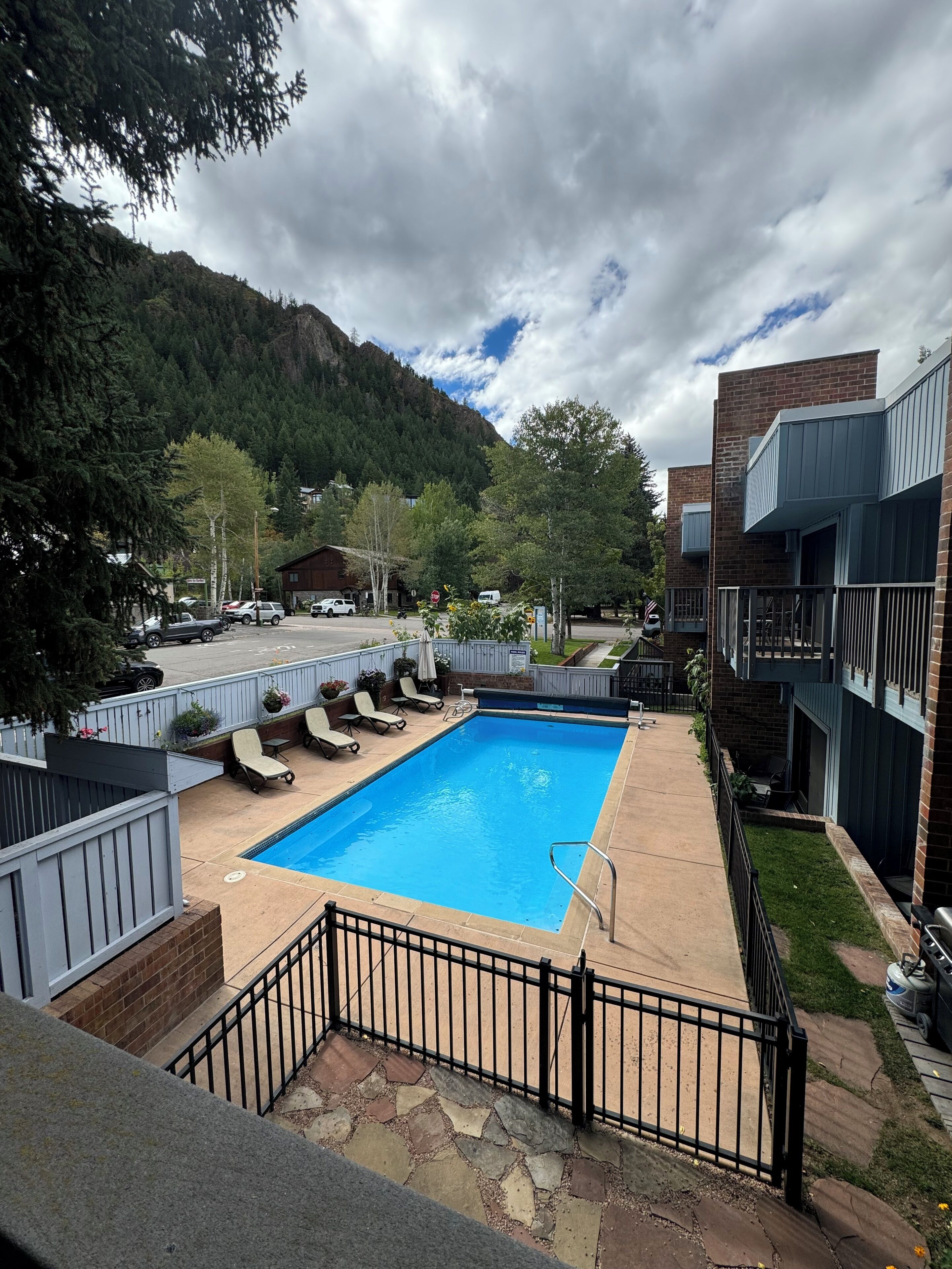 A swimming pool with lounge chairs, surrounded by a fence, with a mountain in the background.