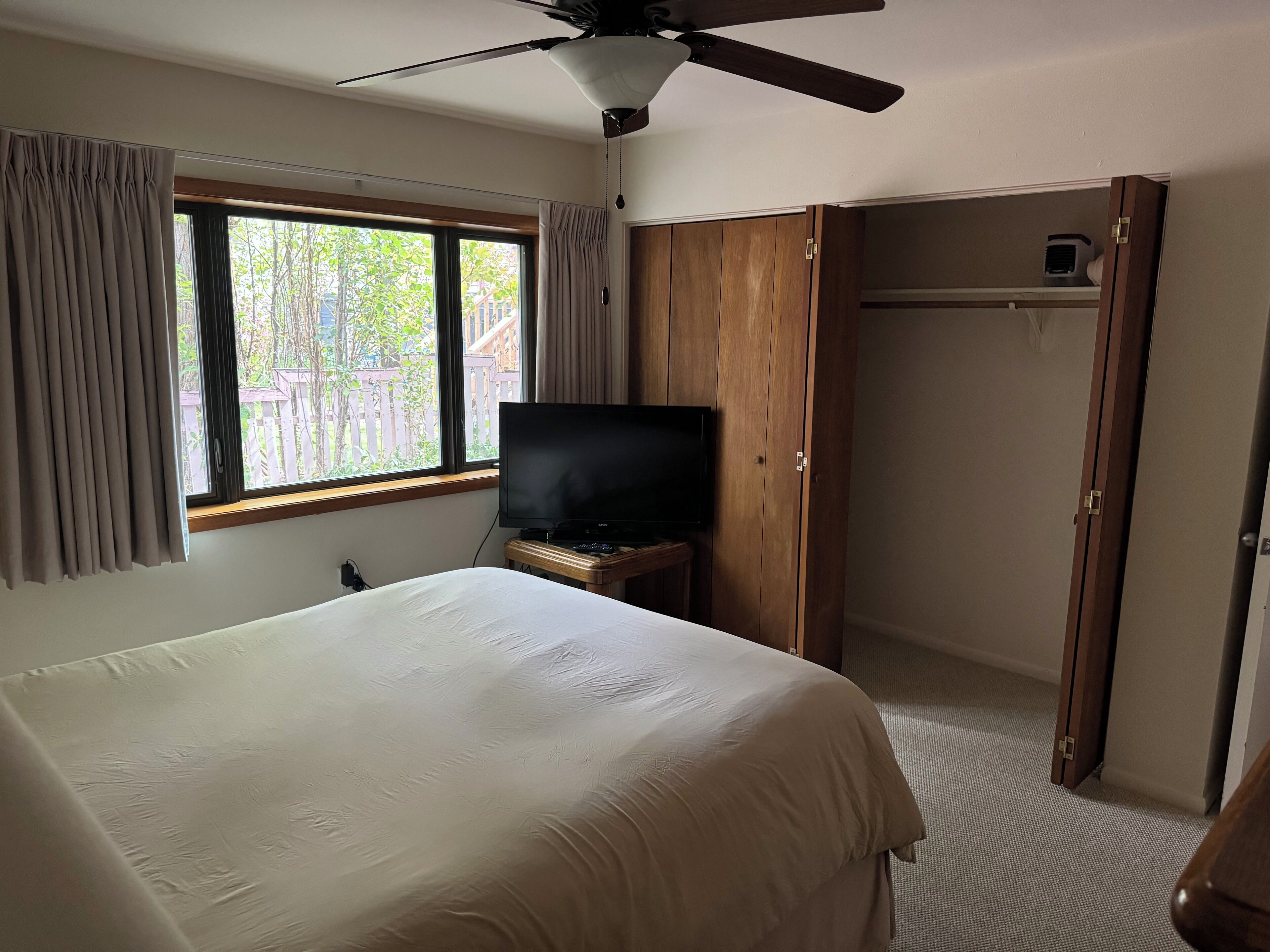 Une chambre à coucher comprenant un lit, une télévision, un ventilateur de plafond et une armoire.