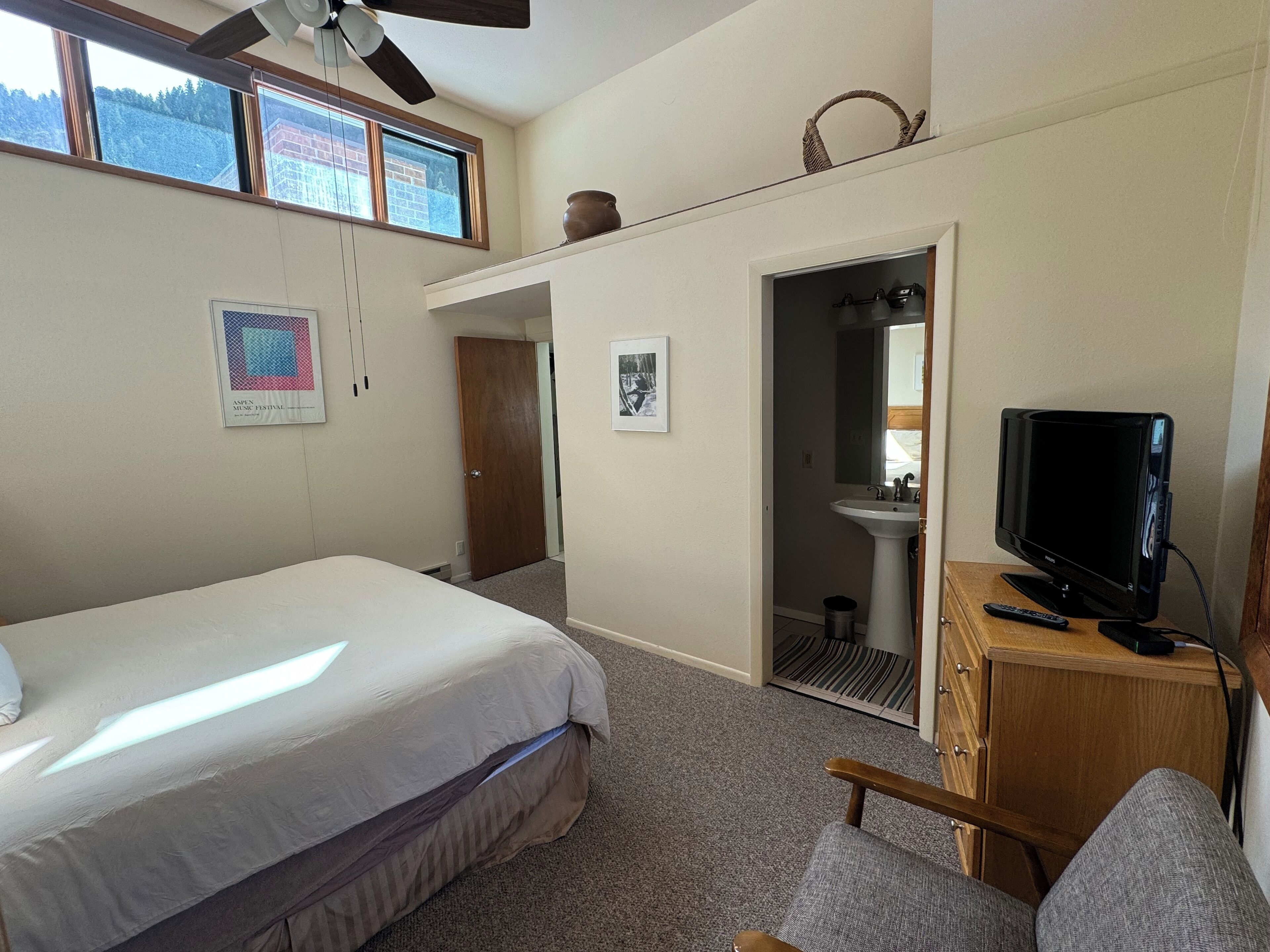 A bedroom with a bed, a television, a wooden cabinet, a bathroom with a sink, and a door leading to another room.