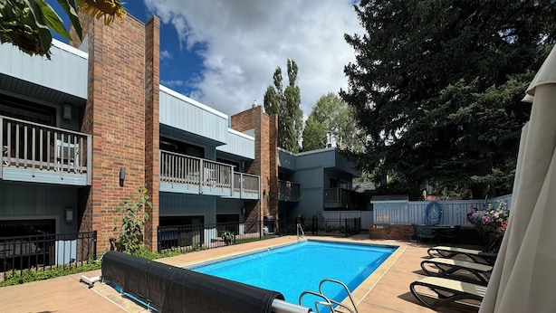 Una piscina con zona cubierta, rodeada por un edificio de ladrillo con balcones y mobiliario de exterior.