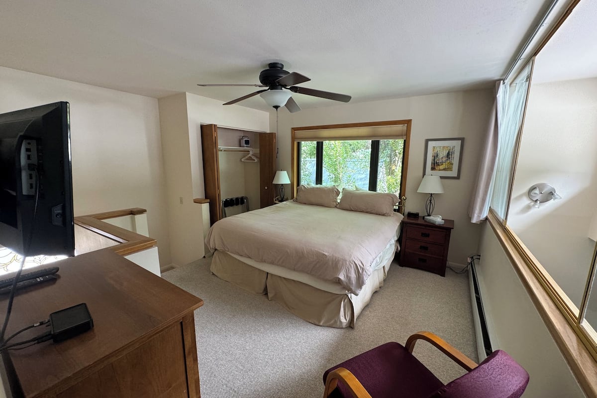 Une chambre à coucher comprenant un lit, un bureau, une chaise, un ventilateur de plafond, une fenêtre et une table de chevet.