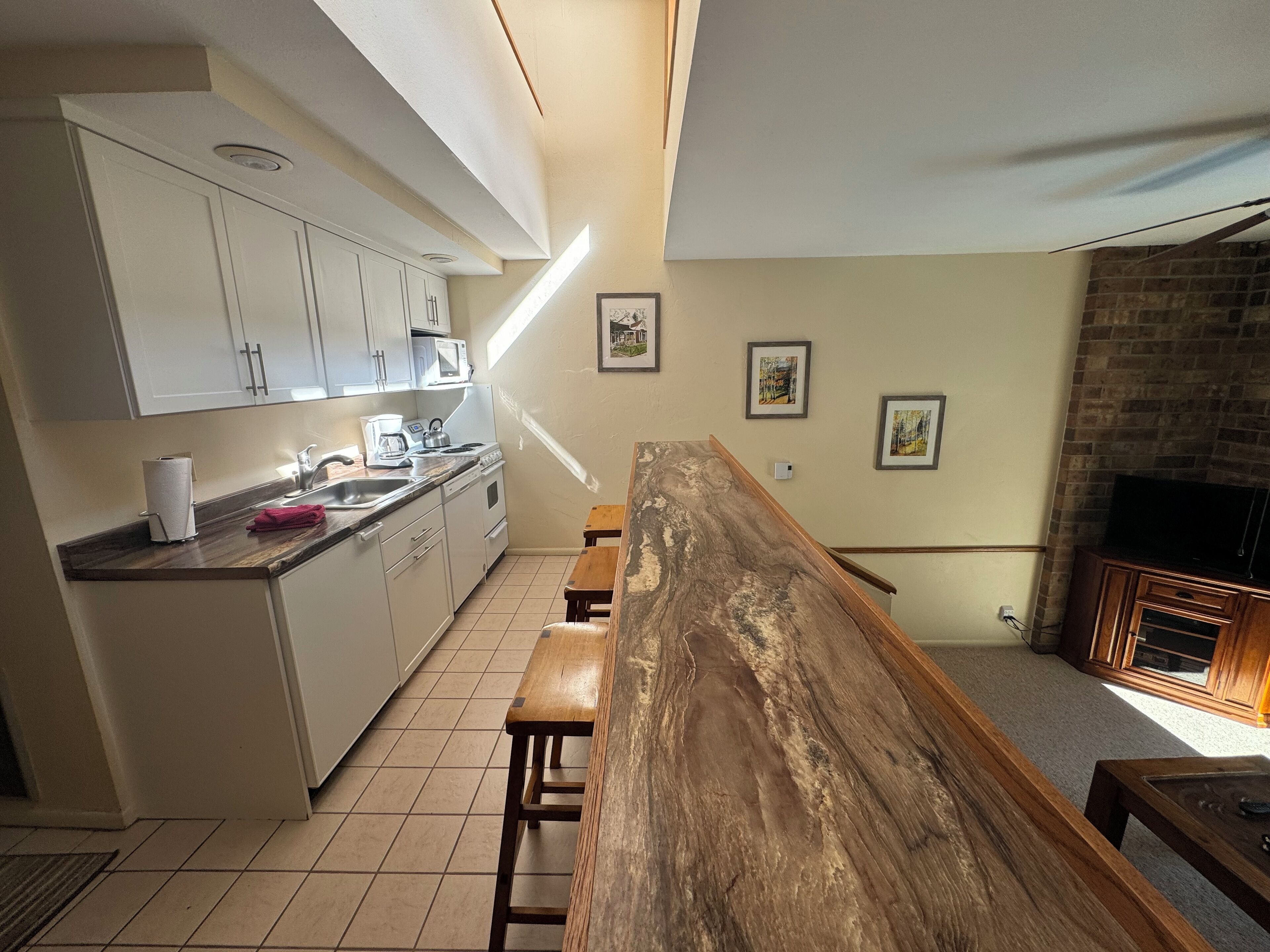 Una cocina con armarios blancos, un banco de madera y una pared de ladrillo.