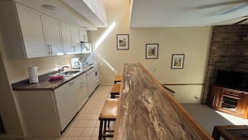 Una cocina con armarios blancos, un banco de madera y una pared de ladrillo.