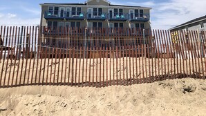 A beachfront property with a multi-story building, a wooden fence, and a clear blue sky. - Misquamicut Beach Front Inn (Westerly)