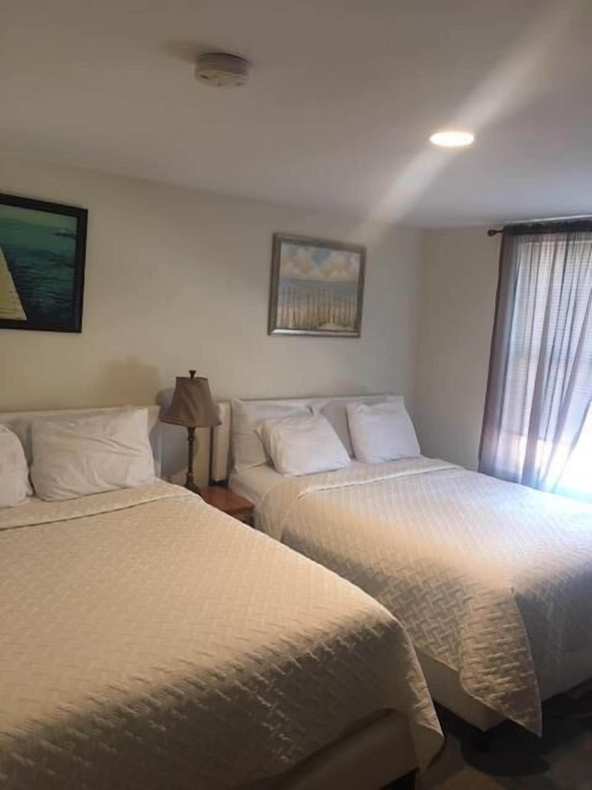 A hotel room with two beds, a nightstand, a lamp, and two paintings on the wall.