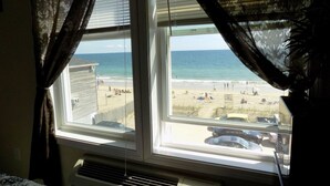 A room with a view of a beach, a window with curtains, and a wall-mounted air conditioner. - Misquamicut Beach Front Inn (Westerly)