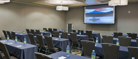 A conference room with tables, chairs, water bottles, a projector screen, and a presentation screen.
