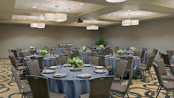 A conference room with round tables, chairs, and a projector on the ceiling.
