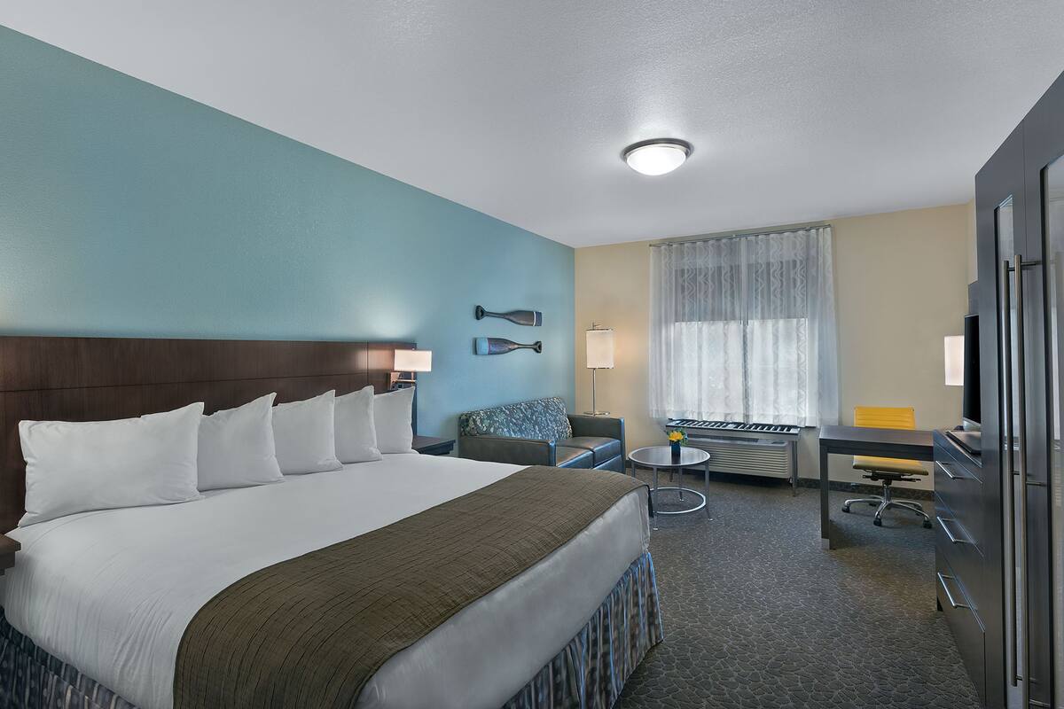 A hotel room with a large bed, a desk, a chair, a lamp, and a window with curtains.