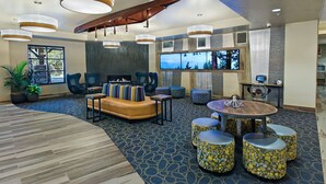 A modern lounge area with a large window, comfortable seating, and a unique ceiling design. - Oxford Suites Bellingham (Bellingham)