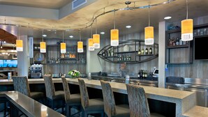 A modern bar area with a long counter, multiple bar stools, hanging pendant lights, and a variety of bottles and glasses on shelves. - Oxford Suites Bellingham (Bellingham)