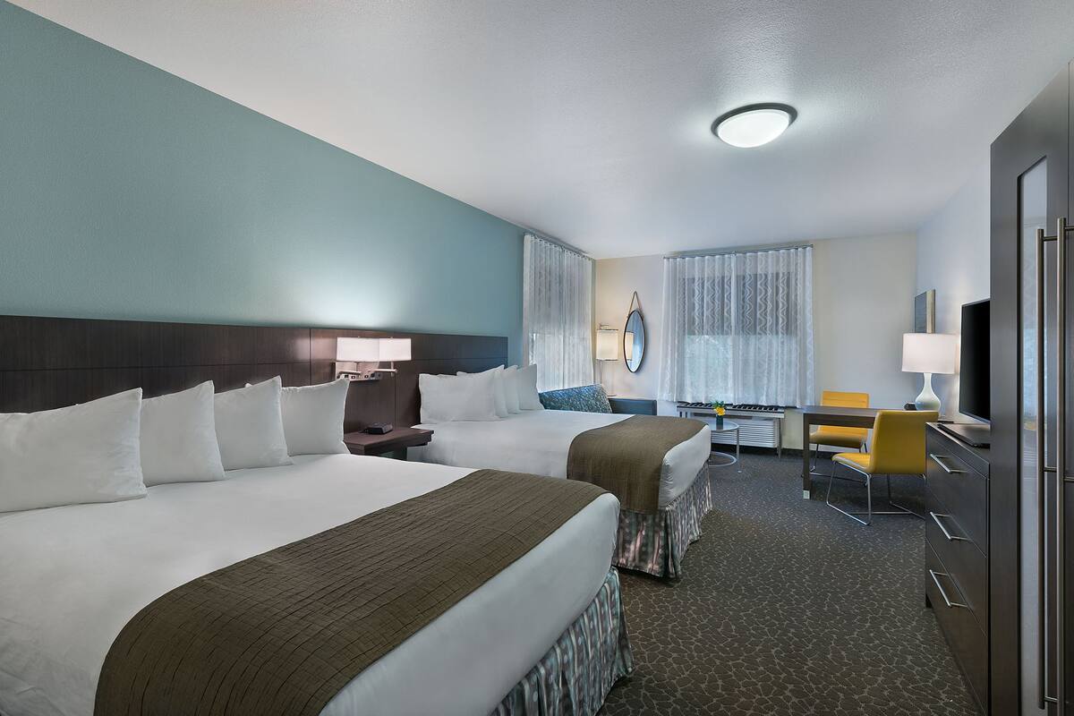 A hotel room with two beds, a desk, a chair, a TV, and a bathroom.