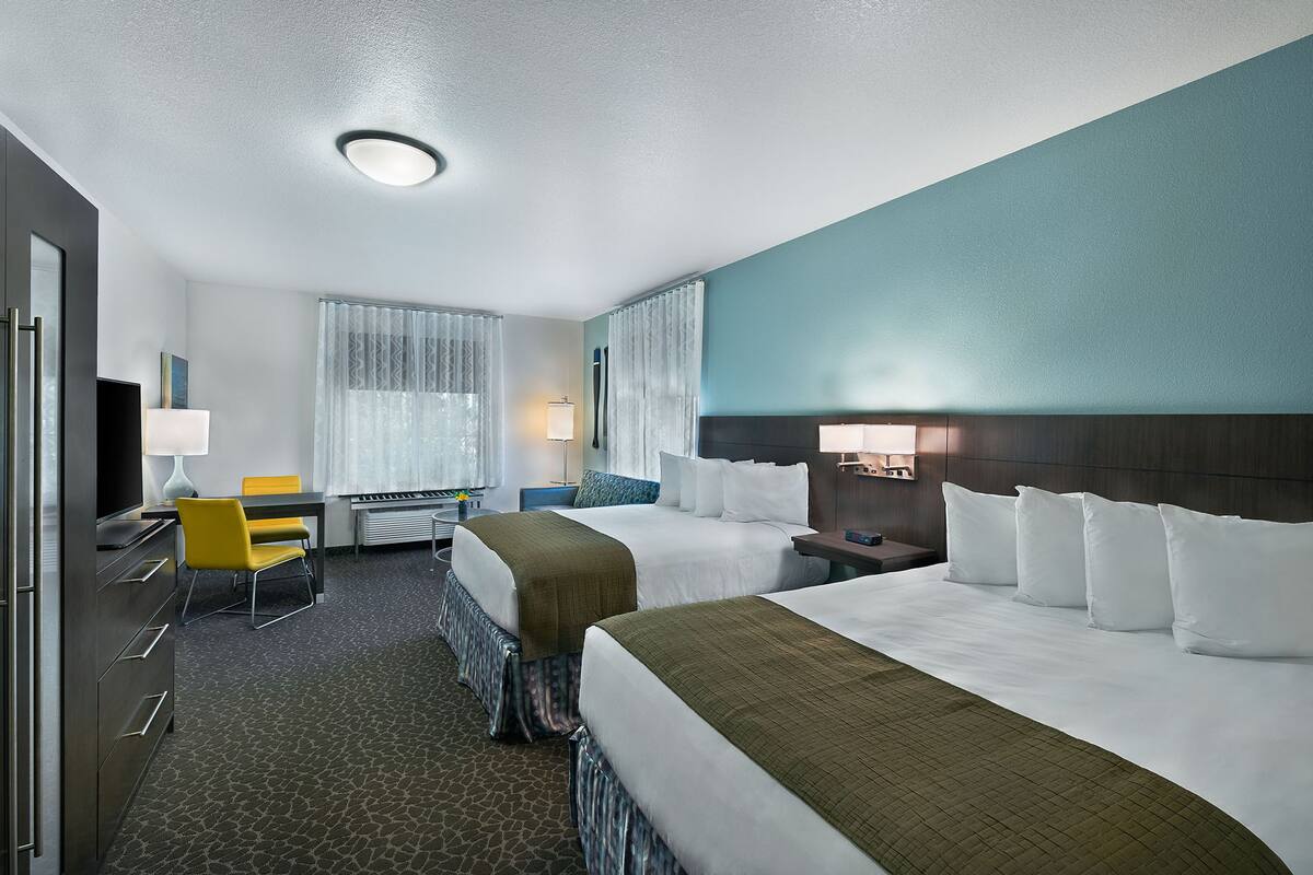 A hotel room with two beds, a desk, a chair, a lamp, and a window with curtains.