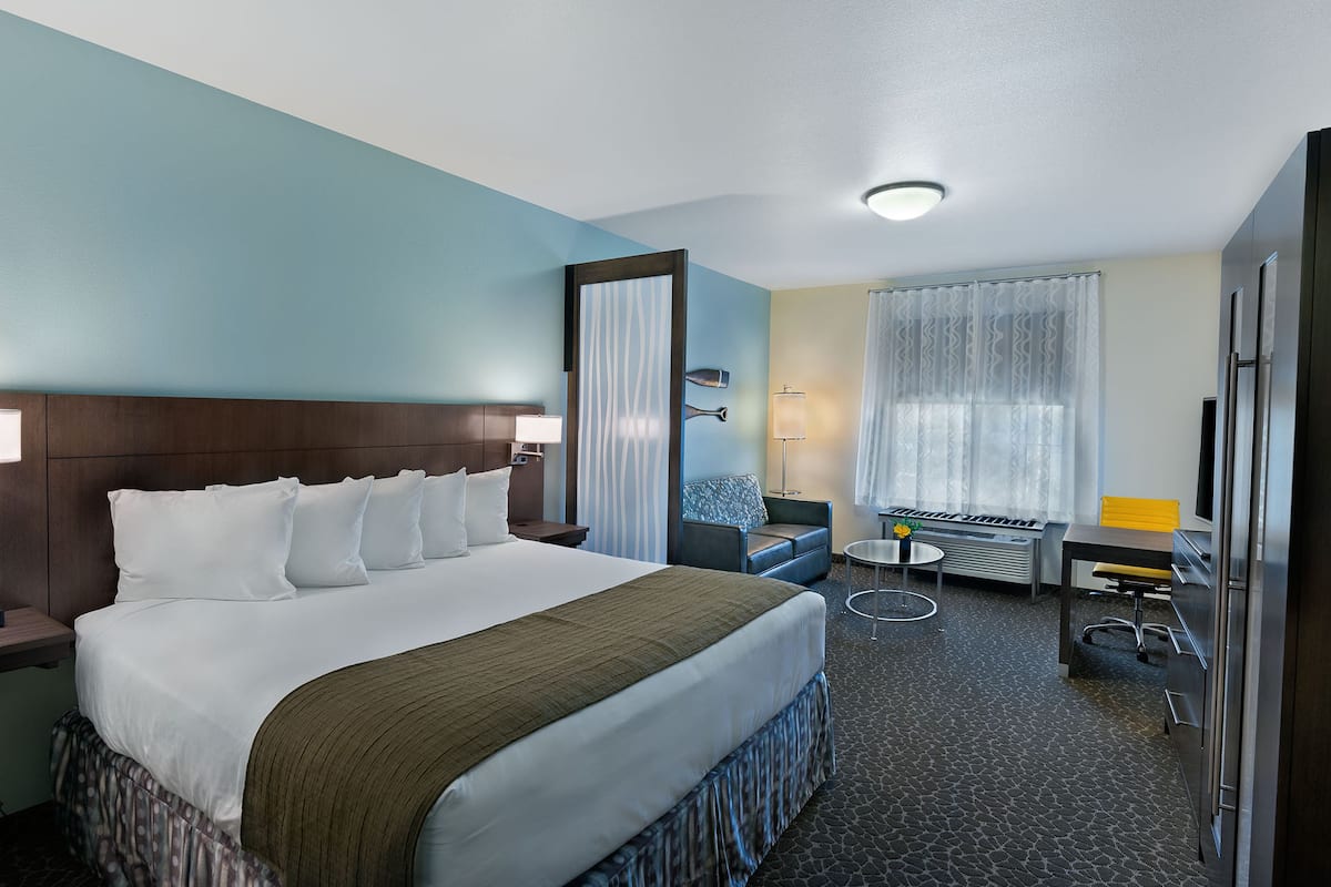 A hotel room with a large bed, a desk, a chair, a lamp, and a window with curtains.