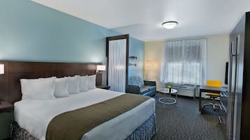 A hotel room with a large bed, a desk, a chair, a lamp, and a window with curtains.