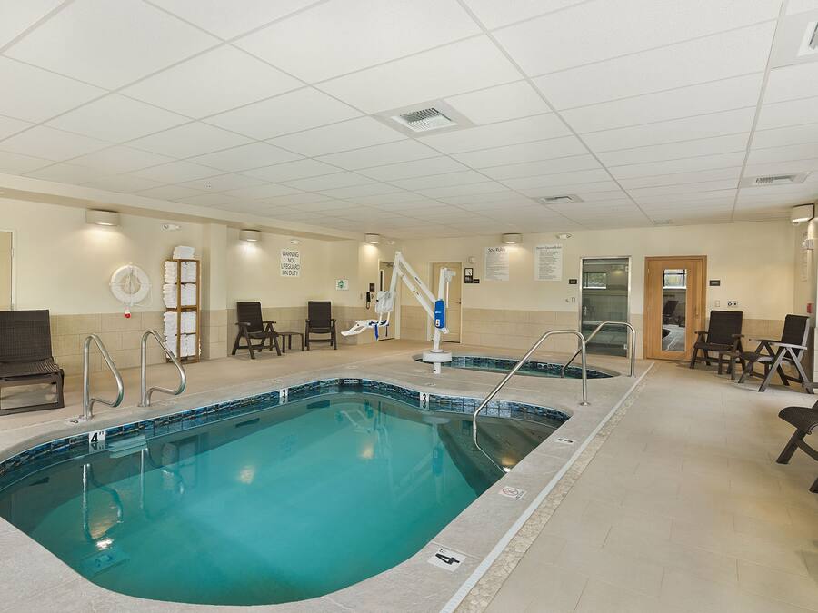 An indoor swimming pool with clear water, surrounded by lounge chairs and a tiled floor.