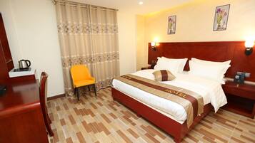A hotel room with a bed, a chair, a desk, and a nightstand.