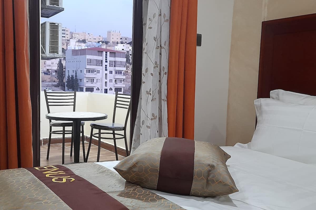 A hotel room with a bed, a small table with two chairs, and a view of the city through a window with curtains.