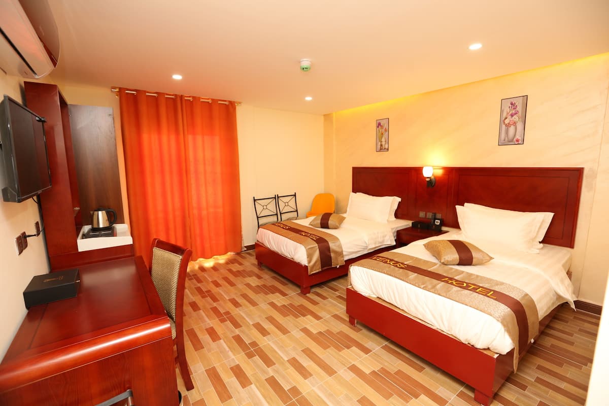 A hotel room with two beds, a desk, a chair, a TV, and a window with curtains.
