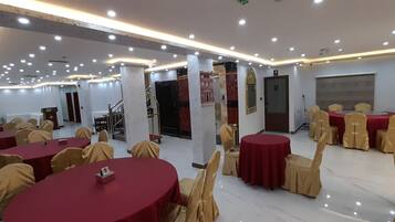 A banquet hall with round tables covered in red tablecloths, arranged in rows.